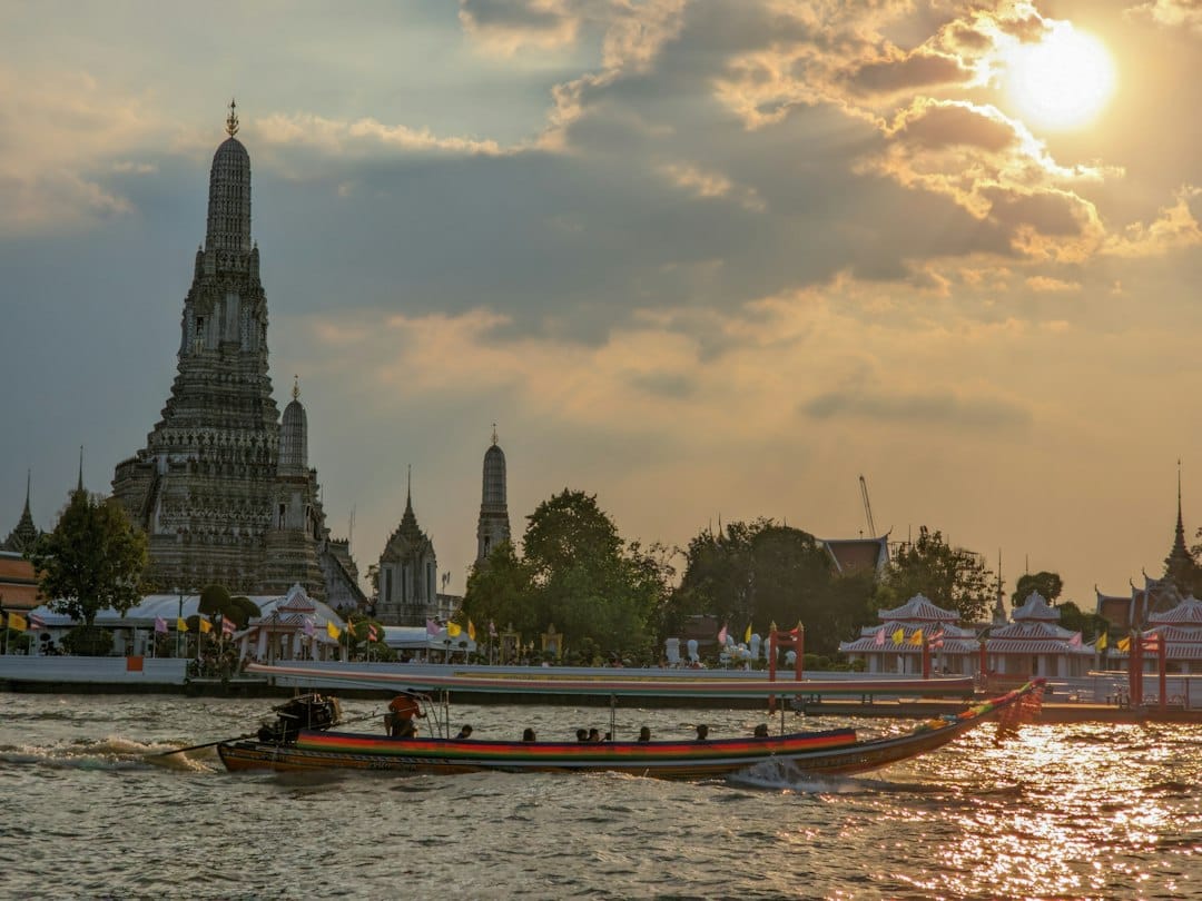 A boat sailing past Wat Arun on the Chao Phraya River in Bangkok at sunset. Photo by Vishal Chokkala on Unsplash