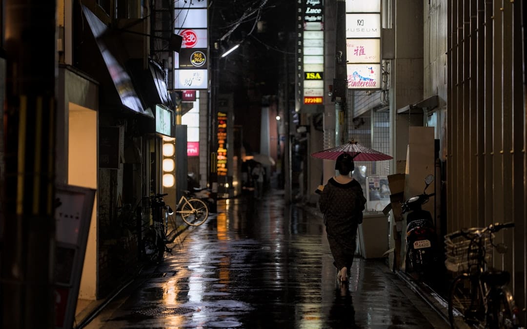 A figure with an umbrella walking down a lantern-lit alley in Gion, Kyoto, at night. Photo by Julien on Unsplash