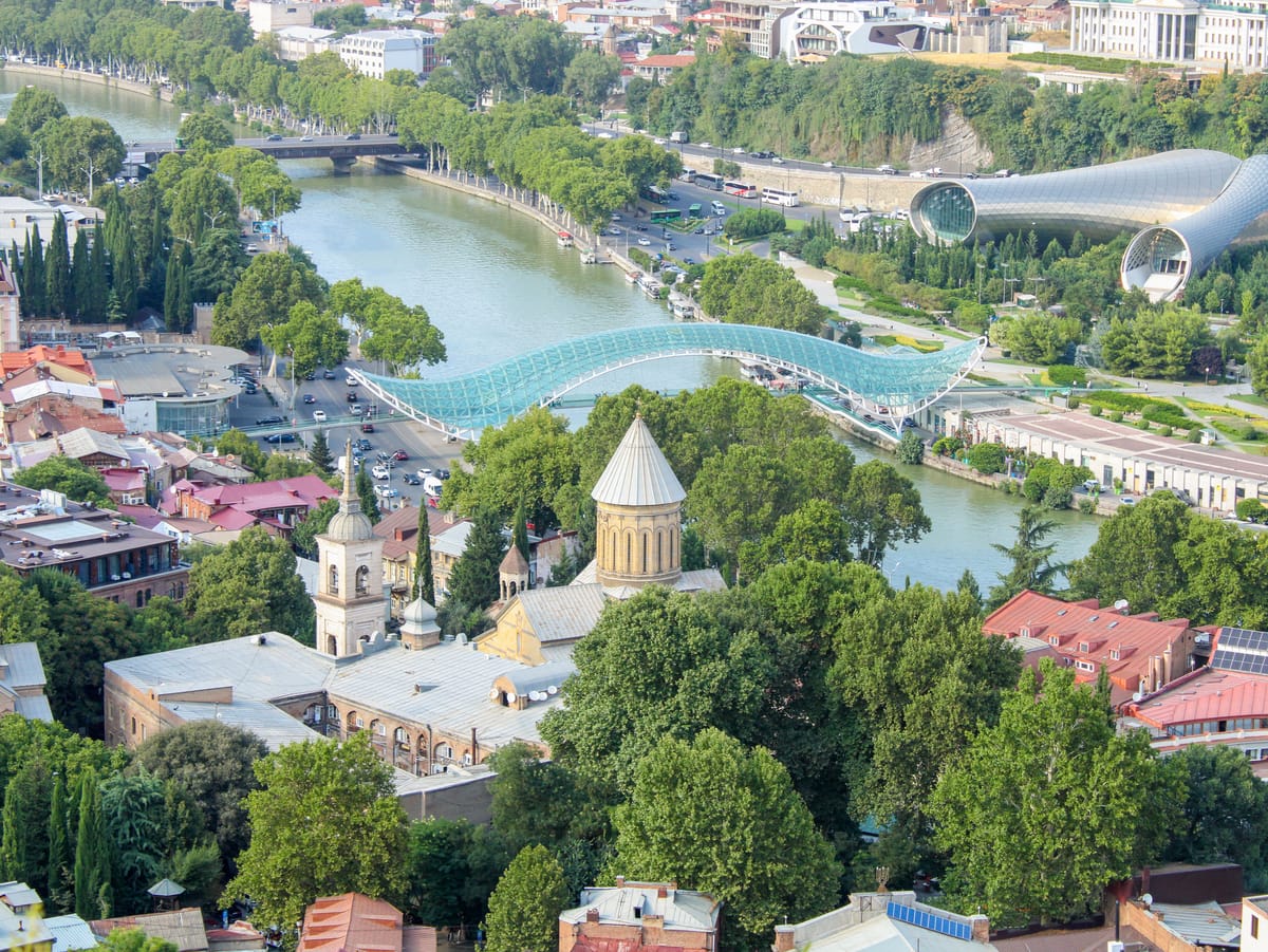 Aerial view of the Bridge of Peace curving over the Mtkvari River in Tbilisi, with Old Town in the foreground